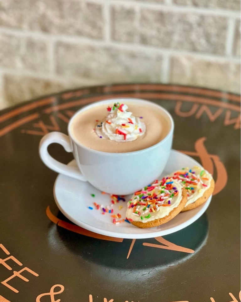 A cup of hot cocoa with whipped cream and sprinkled cookies.