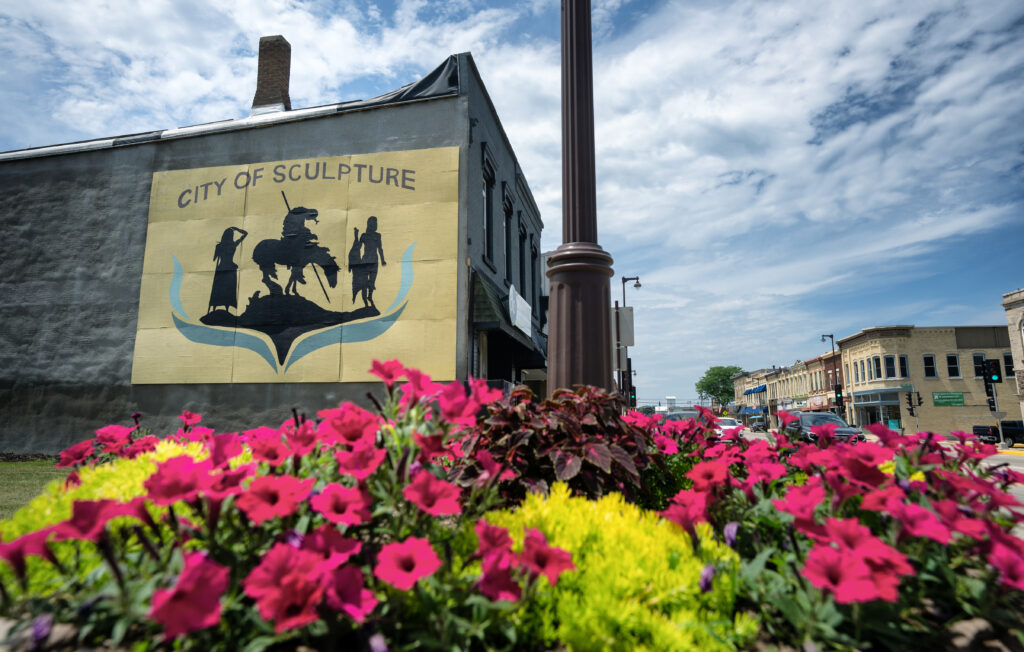 The City of Sculpture mural surrounded by bright flowers downtown.