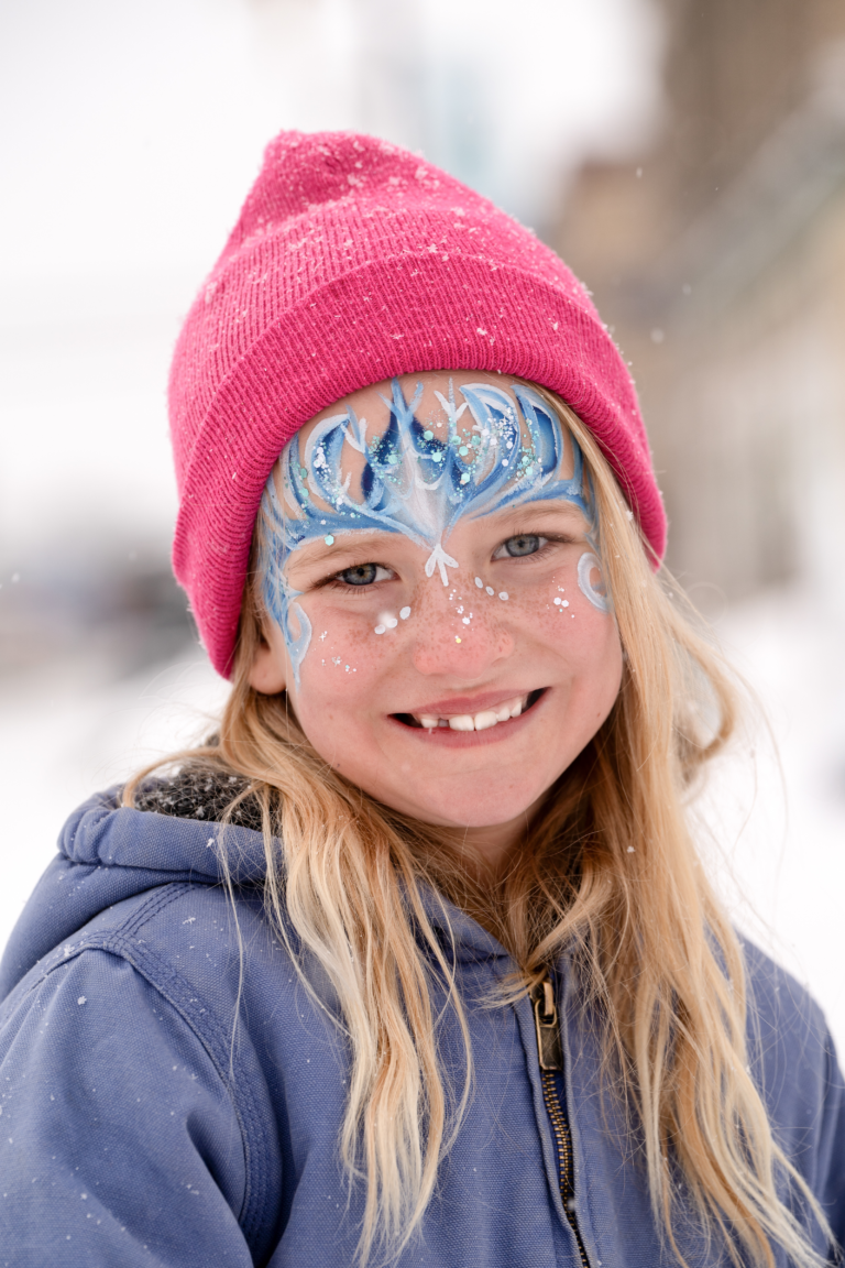 A smiling girl with sparkly winter face paint.