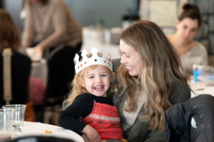 A smiling girl in a paper crown with her mom.